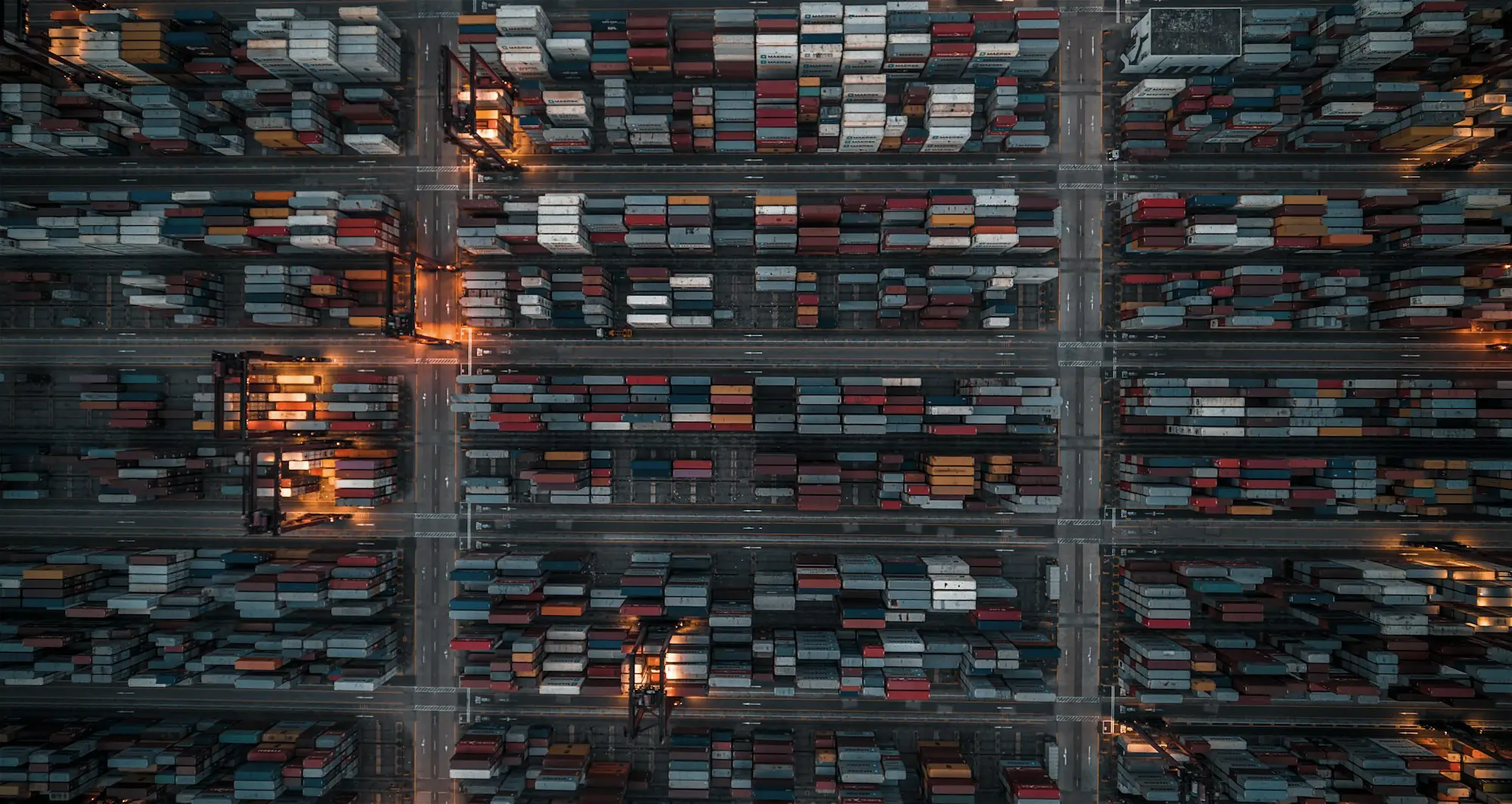 Aerial view of a container terminal at dusk, stacked containers in long rows